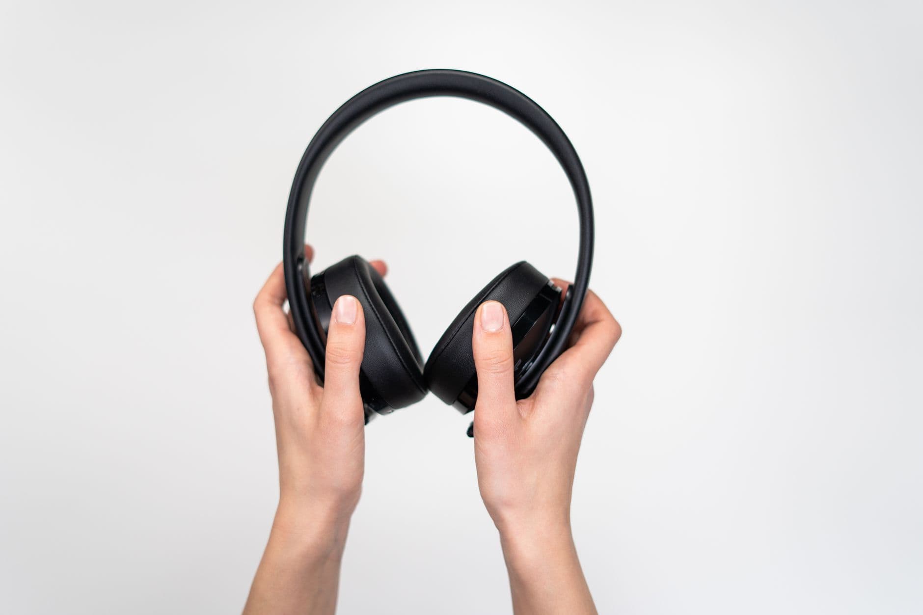 Hands holding over-ear headphones against a plain background