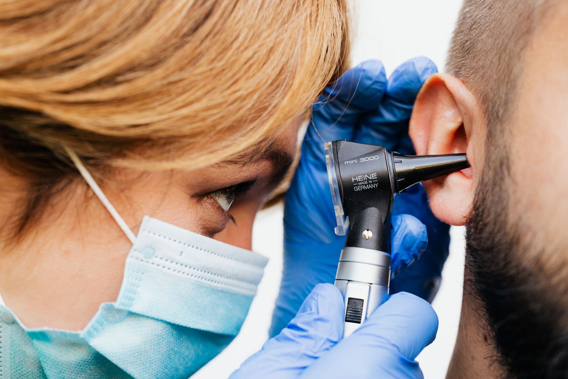 Clinician in gloves examining an ear with an otoscope