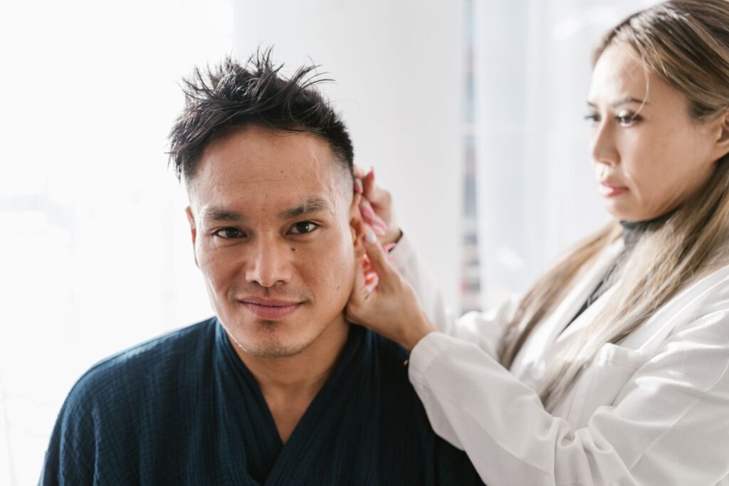 A medical professional performing a thorough ear examination on a seated patient in a bright clinic room.